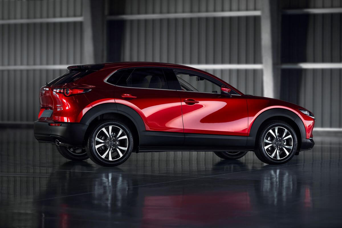 A side profile shot of a red 2023 Mazda CX-30 subcompact crossover SUV model parked in an empty hangar
