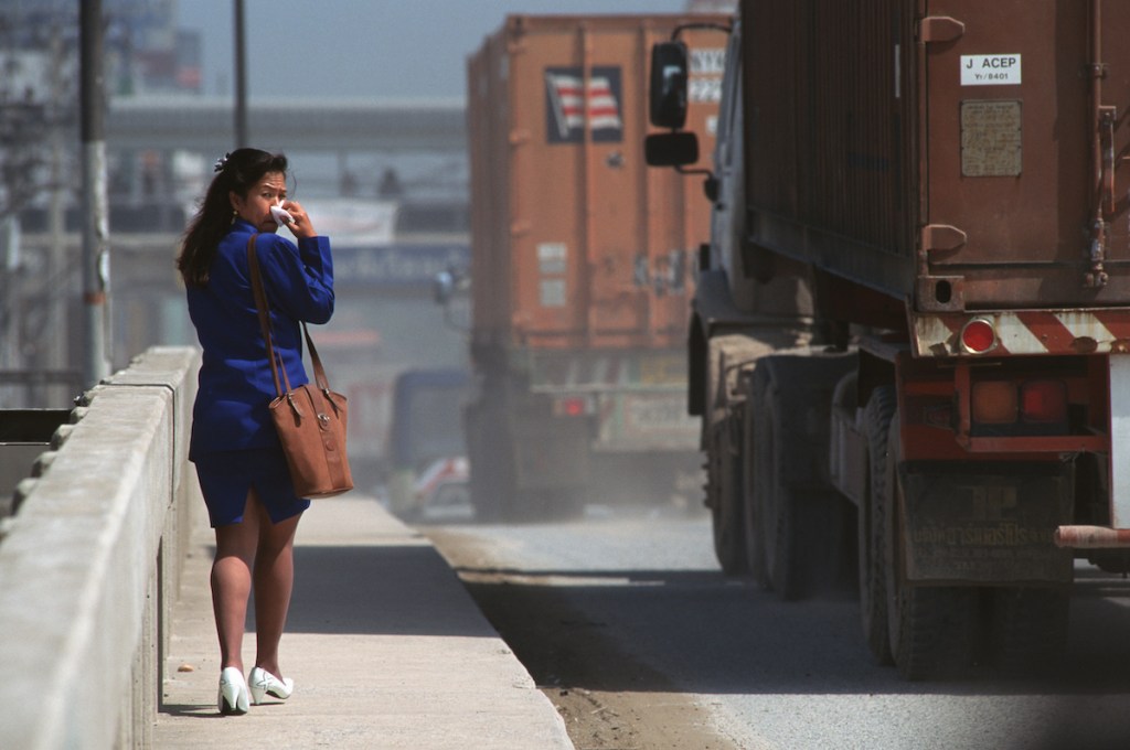 woman covering her mouth as trucks drive by