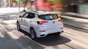 A rear shot of white 2023 Buick Encore GX subcompact SUV model driving through a city with a blurred background