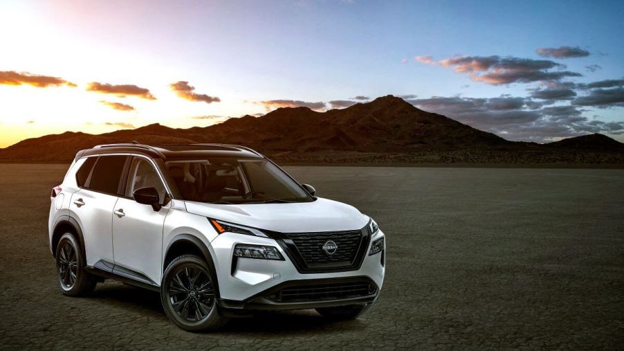 A white 2023 Nissan Rogue compact SUV model parked on dry and empty terrain in front of a sunset above a mountain