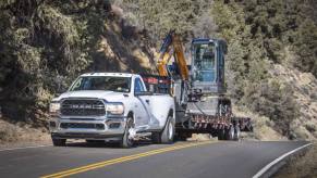 A white 2023 Ram 3500 HD heavy-duty pickup truck model towing a front loader construction excavation vehicle