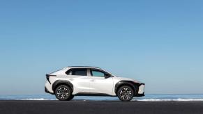 A side profile shot of a 2023 Toyota bZ4X compact electric SUV model in Wind Chill Pearl set against the sea