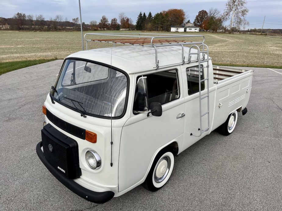 A white Volkswagen T2 bus cut into a pickup truck complete with roof rack, parked in a lot.