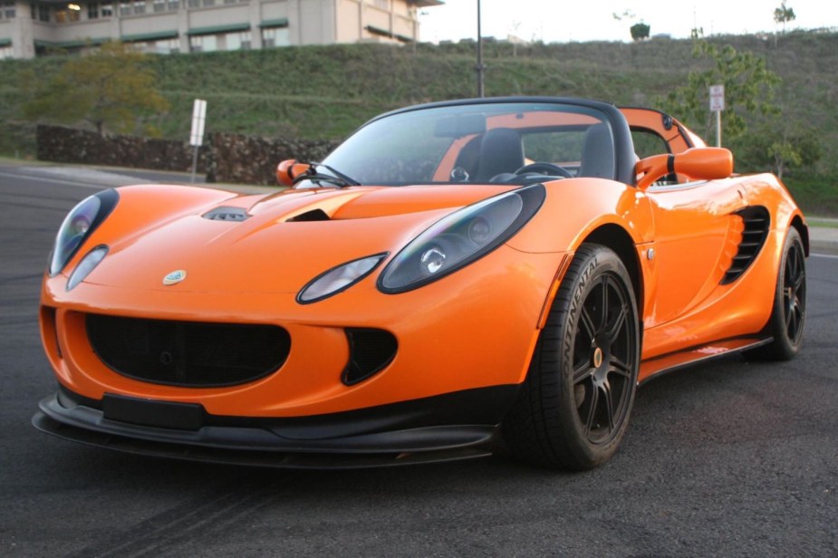 An orange Lotus Elise convertible supercar in a parking lot, tire marks visible all around it.