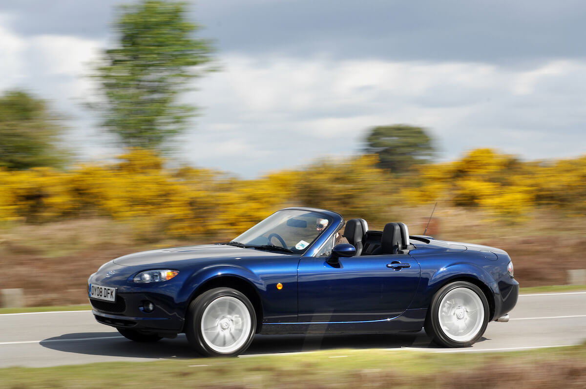 A blue 2008 Mazda MX-5 Miata driving on a country road