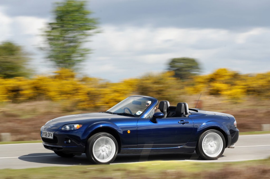 A blue 2008 Mazda MX-5 Miata driving on a country road like those found at Miataland