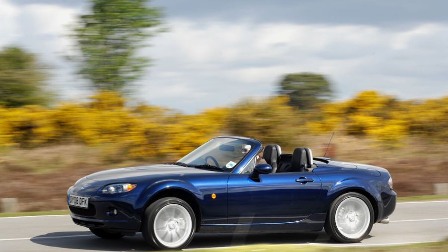 A blue 2008 Mazda MX-5 Miata driving on a country road