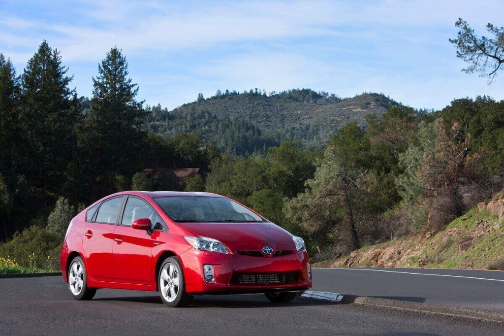A red 2010 Toyota Prius hybrid model parks by a forest. 