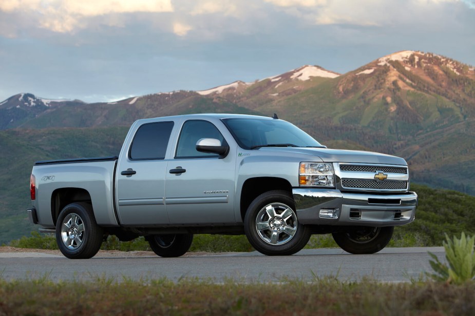 A Chevrolet Silverado hybrid full-size pickup truck parked in front of a row of snow-capped mountains.