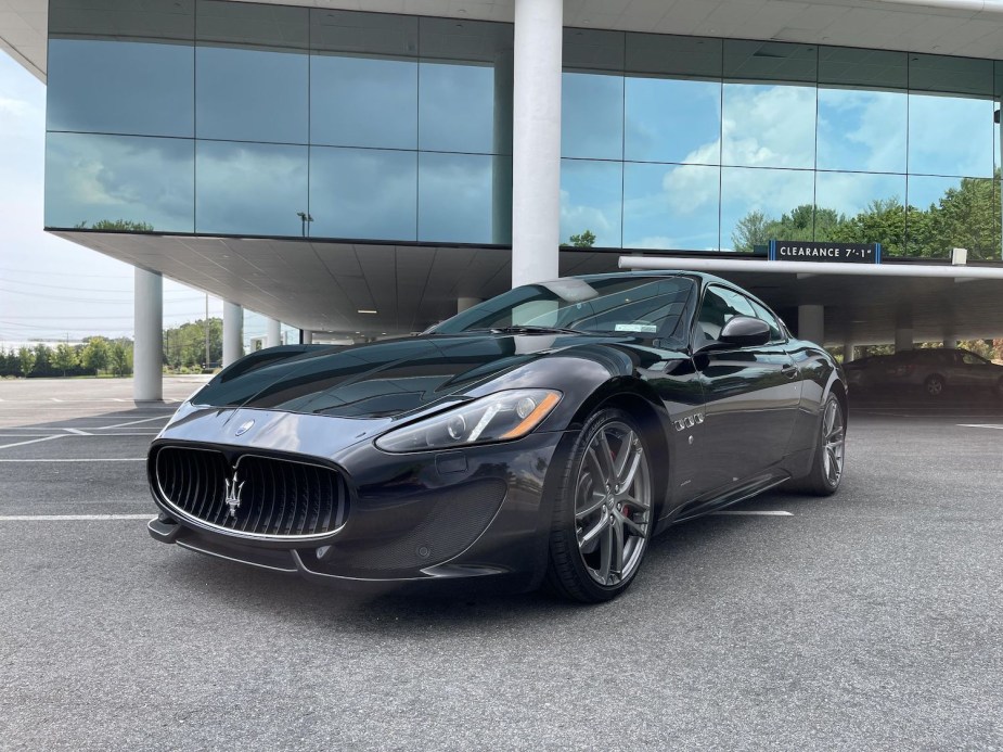 The grille and headlights of a black Maserati Gran Turismo supercar parked in front of a modern glass building.