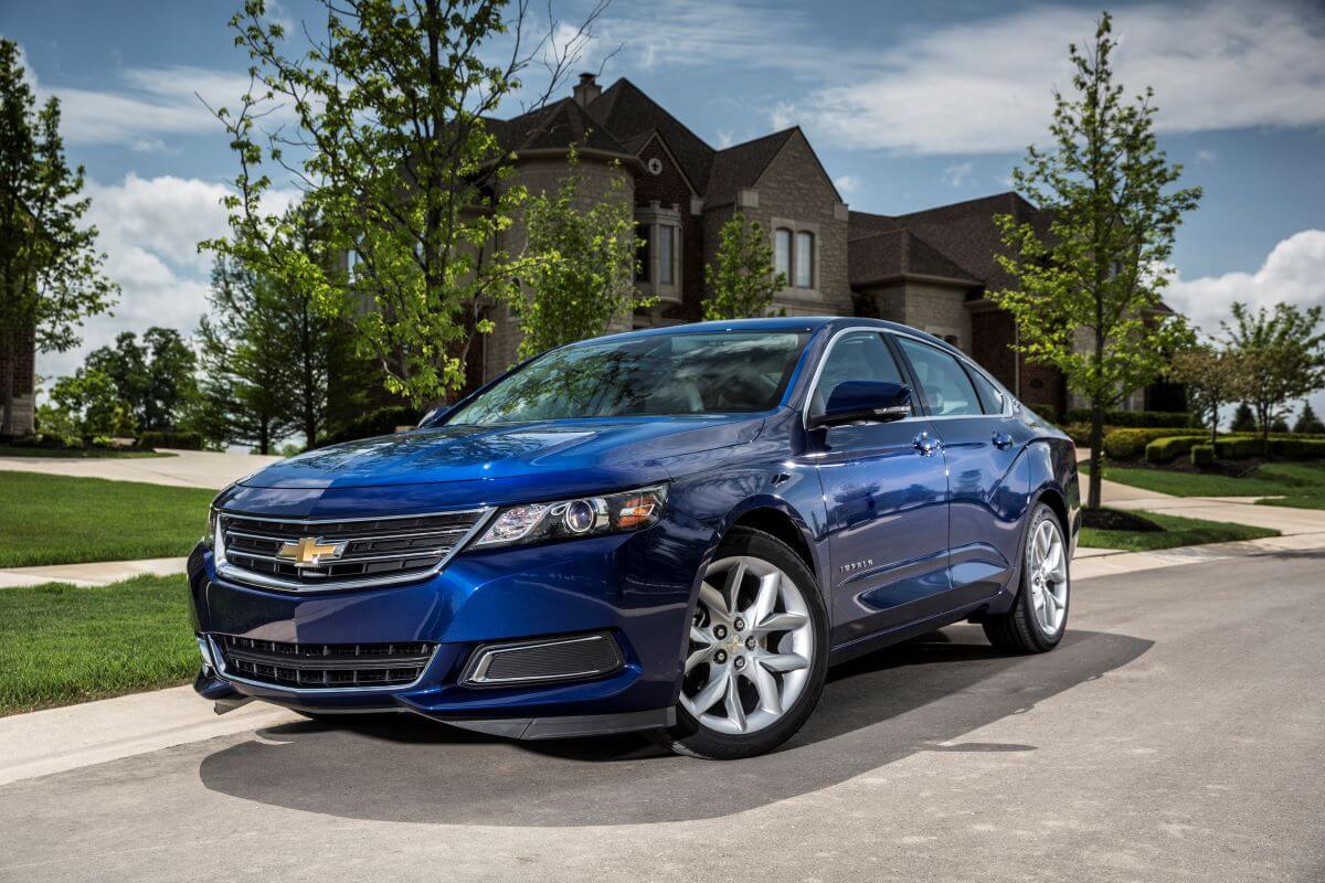 A dark blue 2014 Chevy Impala 2.5L iVLC full-size sedan model parked outside a luxury home