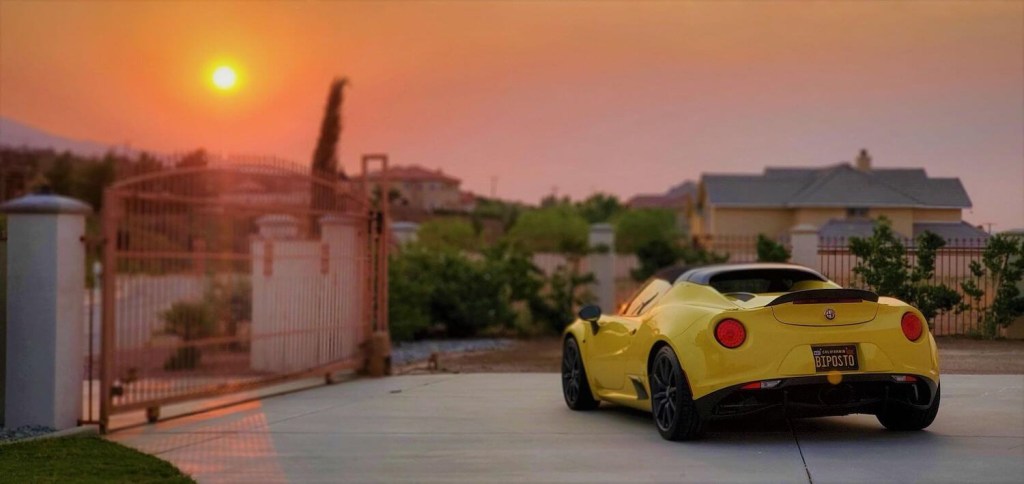 The Alfa Romeo 4C exotic Italian sports car parked in a driveway, the setting sun visible in the background.