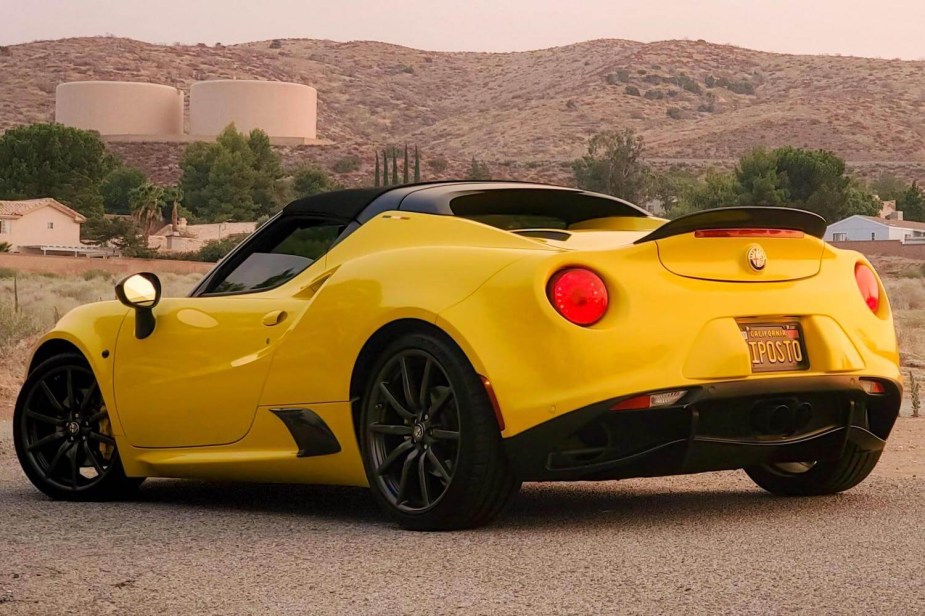 The back of a bright yellow 2015 Alfa Romeo 4C spider, a ridge of mountains visible in the background.