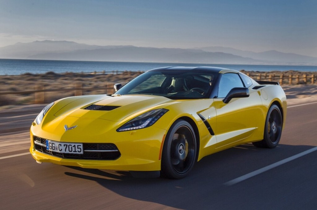 A bright yellow 2015 Chevrolet Corvette C7 cruises down a coastal road with a problem. 