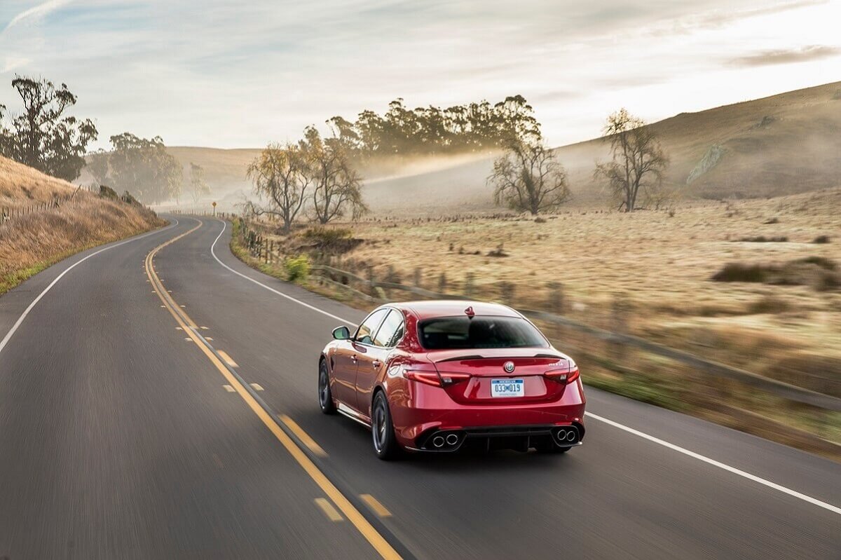 An red Alfa Romeo Giulia without a manual transmission cruises a highway with no other cars.