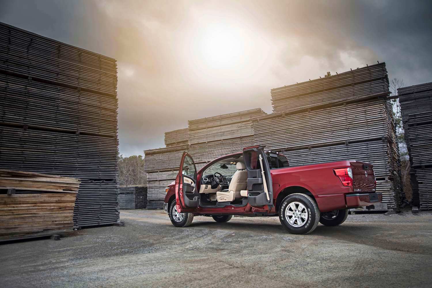 A red Nissan Titan parked in a lumber yard with its rear-hinged rear doors open.