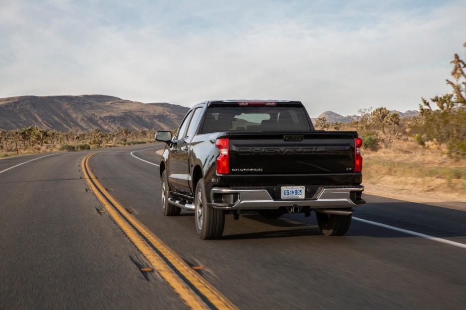 A black Chevrolet Silverado driving away down a rural road, a desert and mountain range visible in the background.