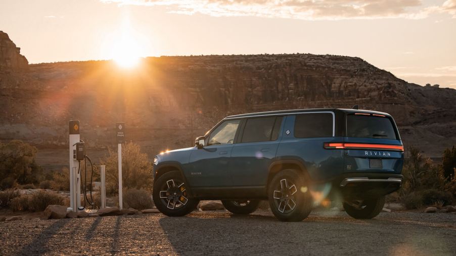 A blue Rivian R1S charging outside at the sunset in front of some mountains.