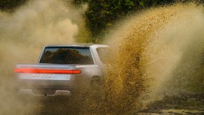 A Rivian R1T electric truck racing across a dirt road, dust visible in the foreground.