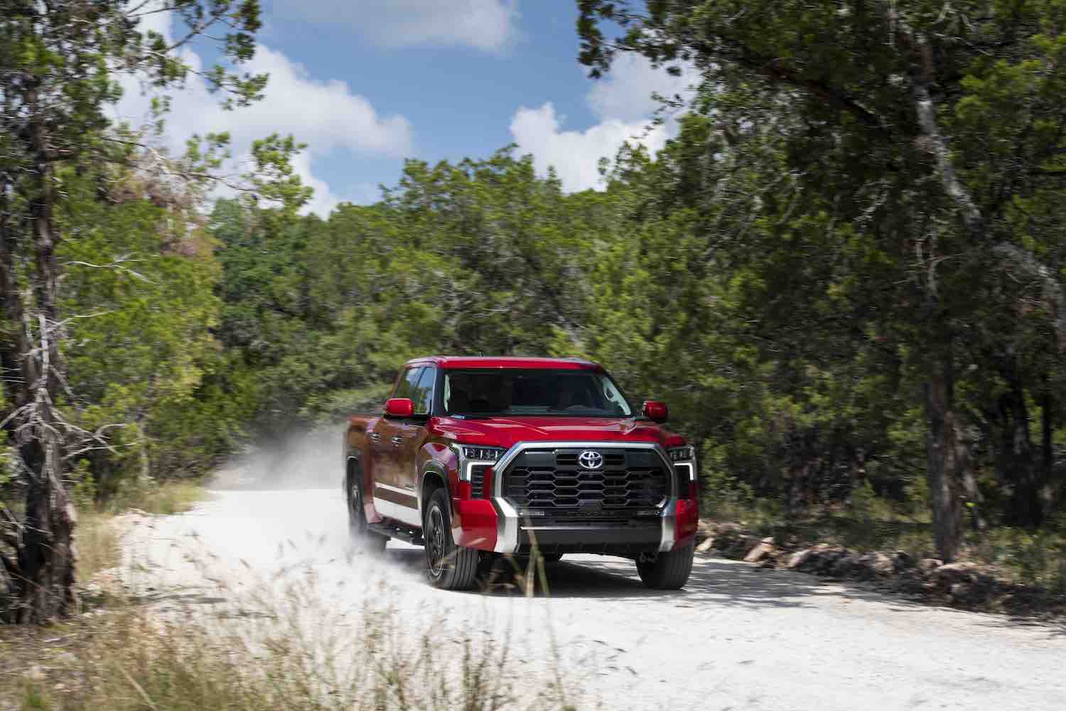 Red 2022 Toyota Tundra pickup truck driving down a dirt road, dust visible behind it.