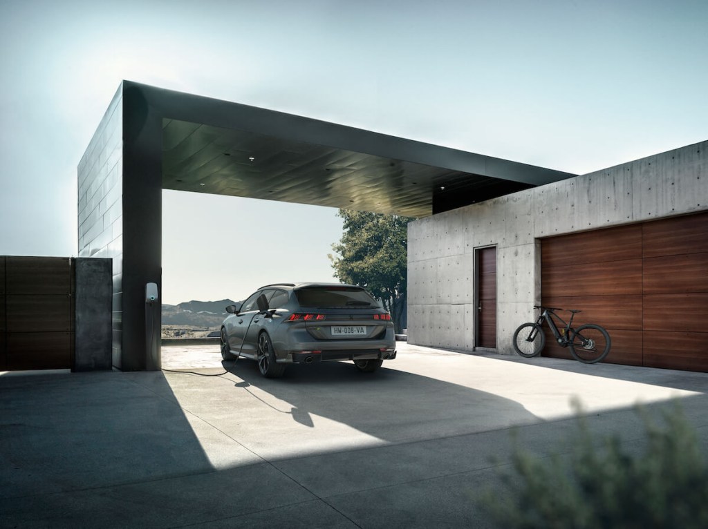 A gray 2023 508 Peugeot Sport wagon parked with the charger plugged in