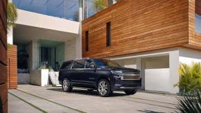 The 2023 Chevy Suburban, the biggest 2023 SUVs, in black parked in front of a modern building with wood accents.