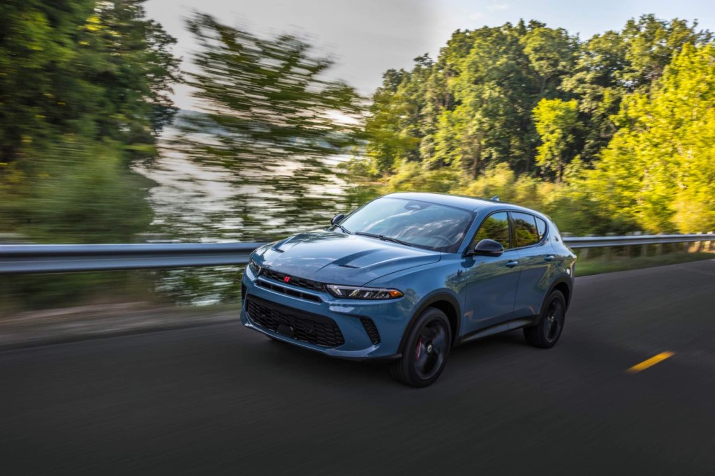 A blue 2023 Dodge Hornet GT drives quickly with green trees in the background.