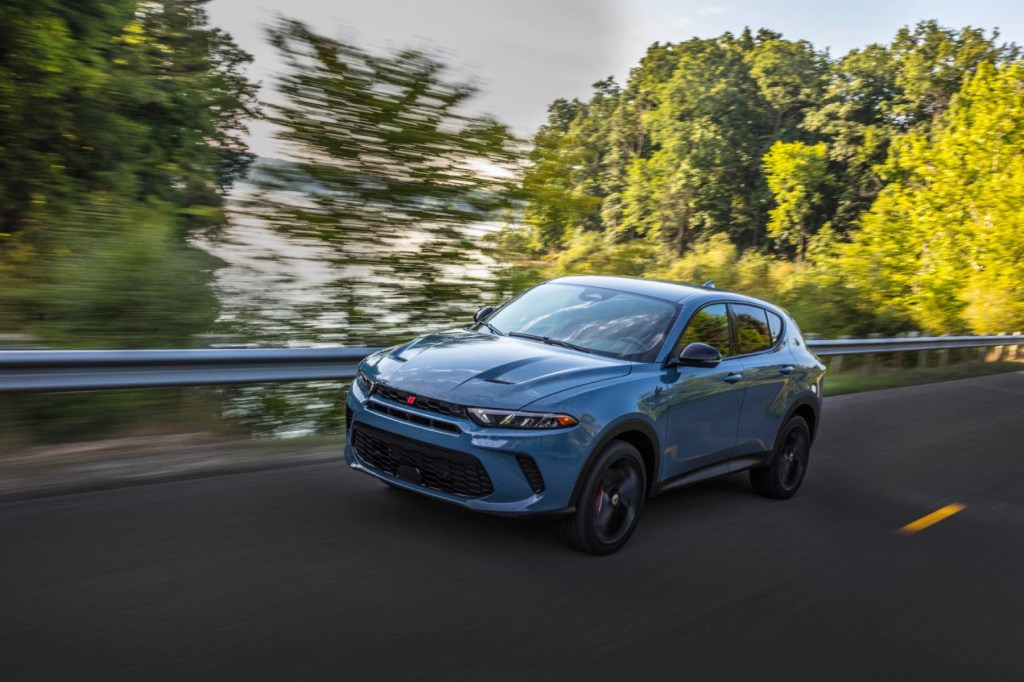 A blue 2023 Dodge Hornet GT drives quickly with green trees in the background. 