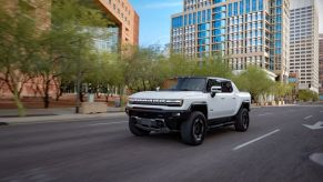 A white 2023 GMC Hummer EV Edition1 all-electric pickup truck model driving on a city road with Super Cruise
