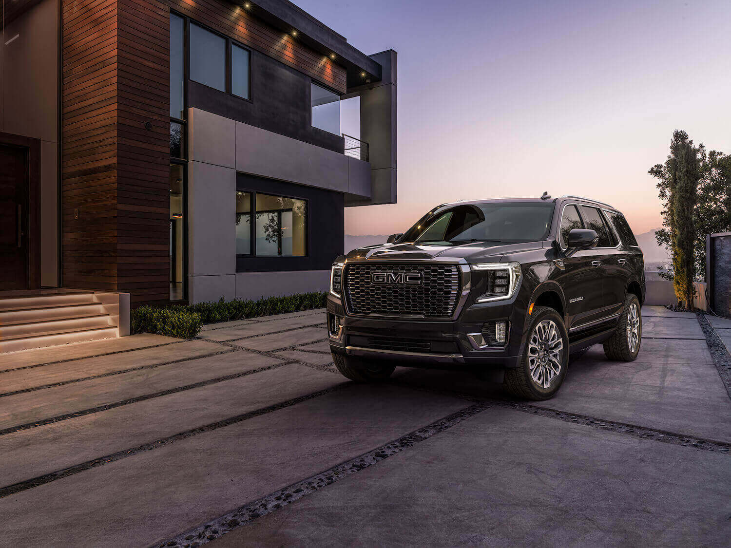 The 2023 GMC Yukon Denali Ultimate exterior in front of a modern building at dusk.