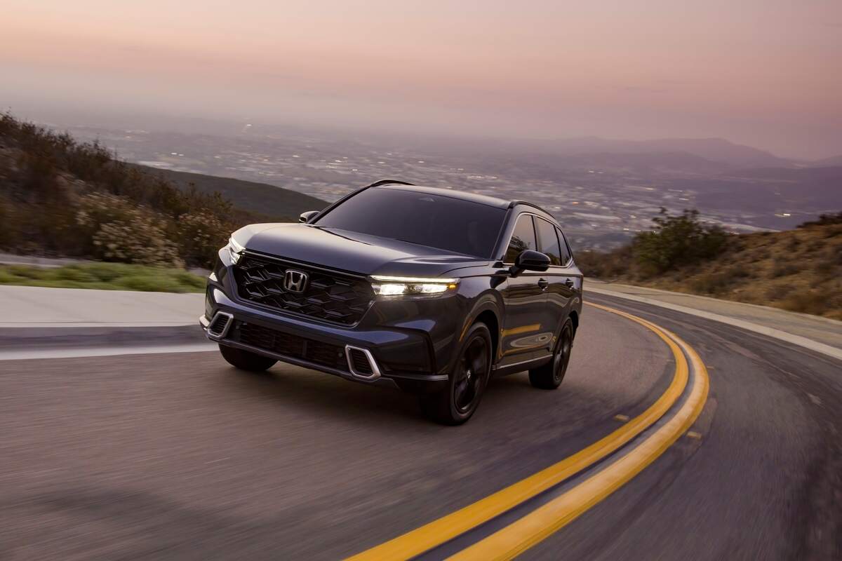 A black 2023 Honda CR-V Sport Touring SUV traveling uphill on a two-lane highway