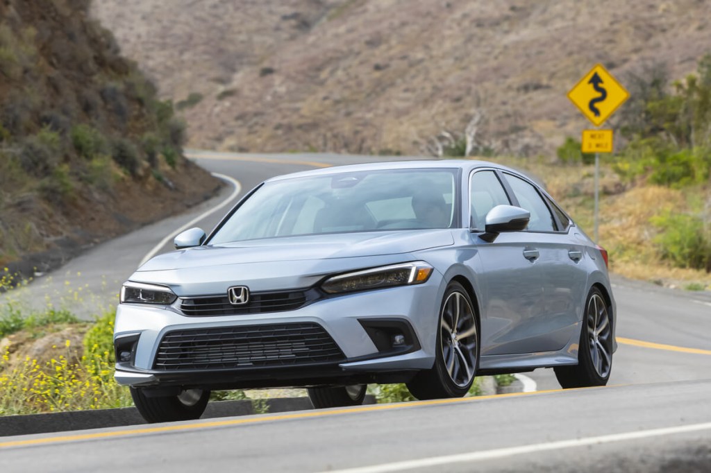 A new silver 2023 Honda Civic corners on a mountain road away from any other cars. 