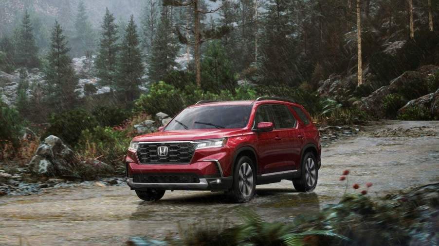 A red 2023 Honda Pilot Elite midsize SUV parked on a mountain road amid pine trees in the rain