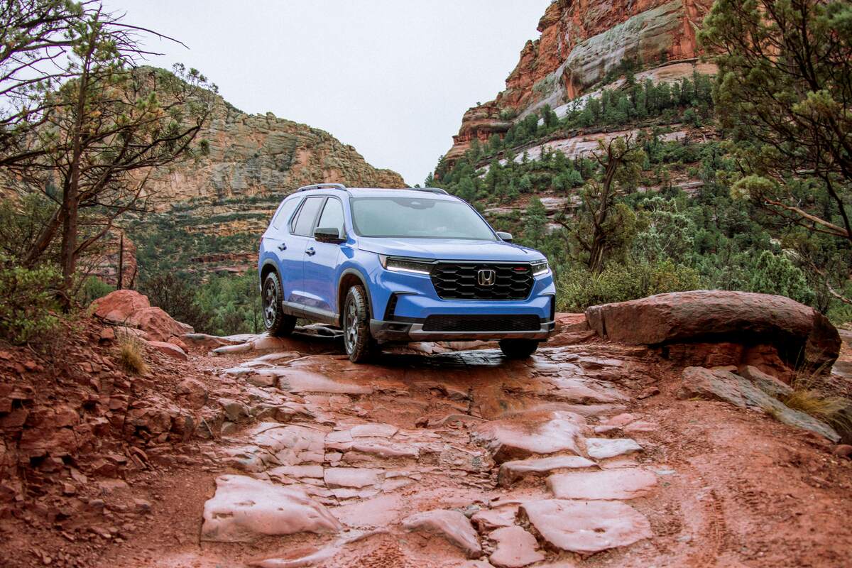 A blue 2023 Honda Pilot TrailSport SUV parked on a red rocks in front of mountains on a cloudy day