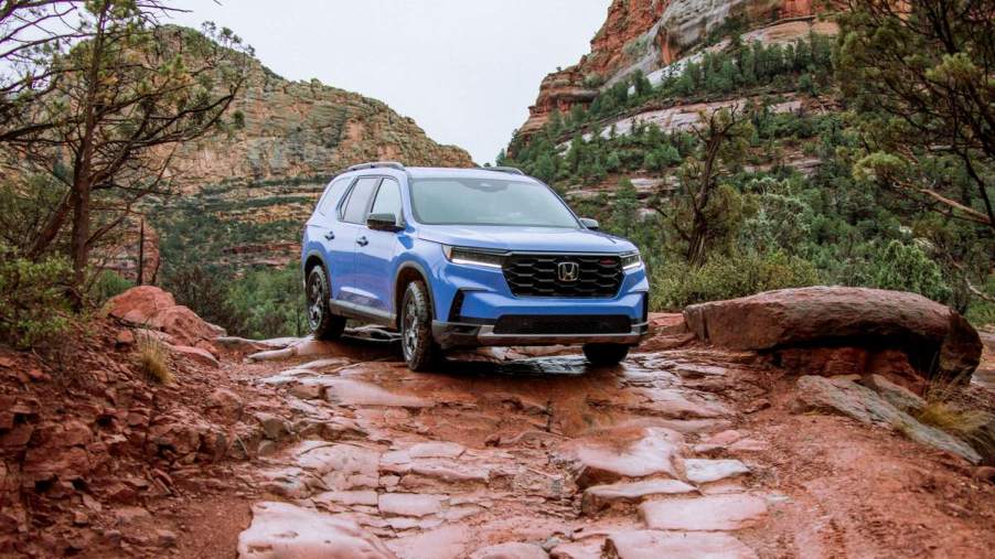 A blue 2023 Honda Pilot TrailSport SUV parked on a red rocks in front of mountains on a cloudy day