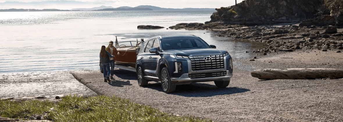 A 2023 Hyundai Palisade Calligraphy midsize SUV model towing a boat on a beach near the sea