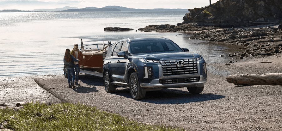 A 2023 Hyundai Palisade Calligraphy midsize SUV model towing a boat on a beach near the sea