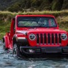 A red 2023 Jeep Wrangler small SUV is driving through water.