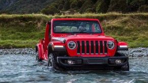 A red 2023 Jeep Wrangler small SUV is driving through water.