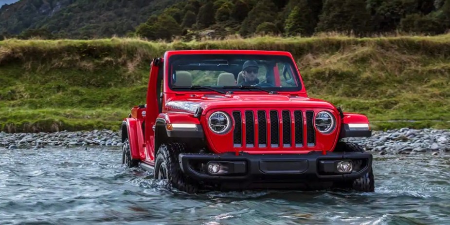 A red 2023 Jeep Wrangler small SUV is driving through the water. 