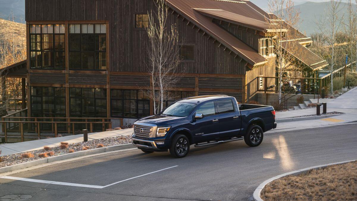 A blue 2023 Nissan Titan full-size pickup truck driving past a large wooden resort building