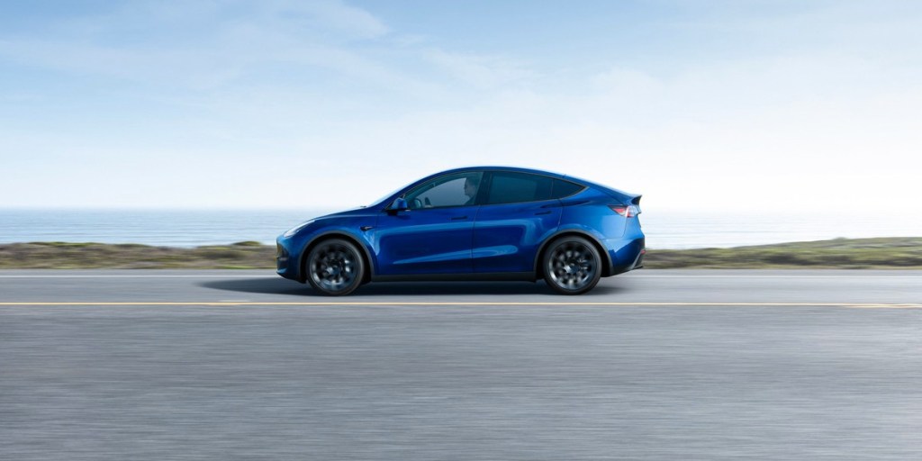 A blue 2023 Tesla Model Y small electric SUV is driving on the road.