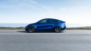 A blue 2023 Tesla Model Y small electric SUV is driving on the road.