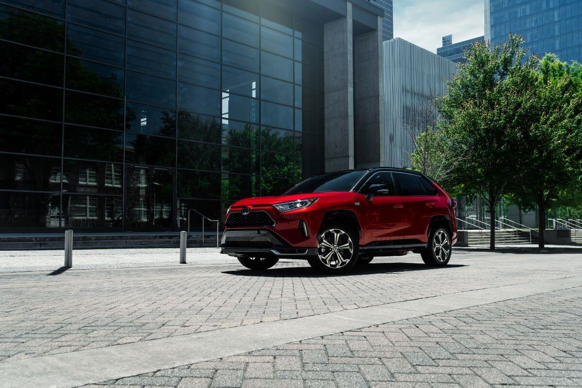 A red 2023 Toyota RAV4 Prime XSE plug-in hybrid electric vehicle (PHEV) model outside a glass office building