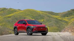 A red Subaru Solterra parked on a road with a green hill in the background.