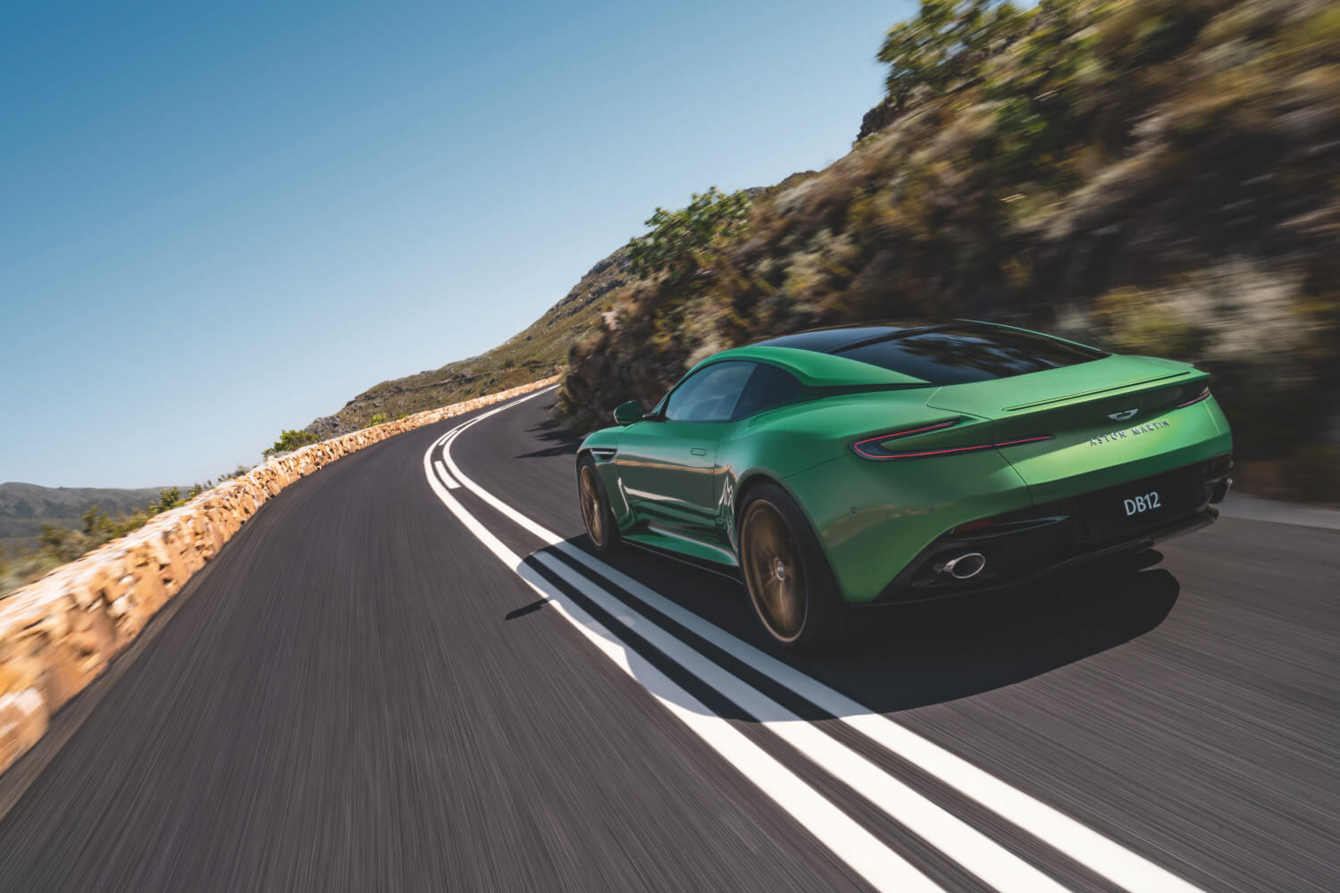 The back of a green Aston martin DB12 as it races along a mountain road.