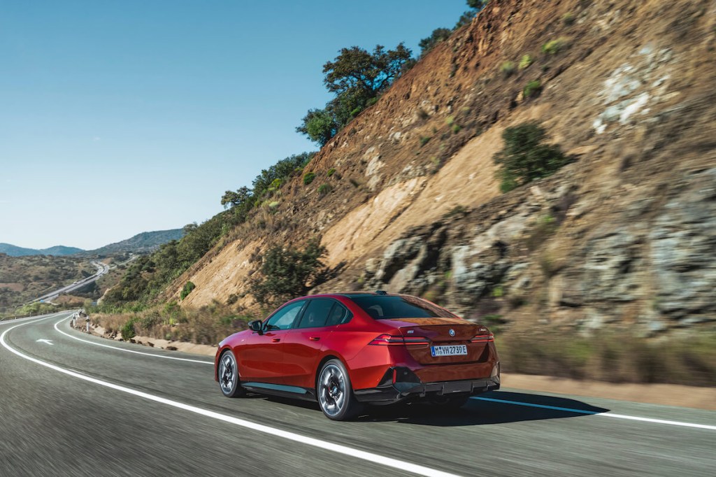 A red 2024 BMW I5 M60 driving down a road in the mountains