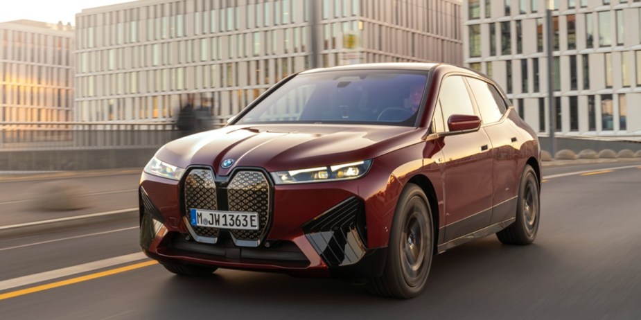 A red 2024 BMW iX midsize electric SUV is driving on the road. 