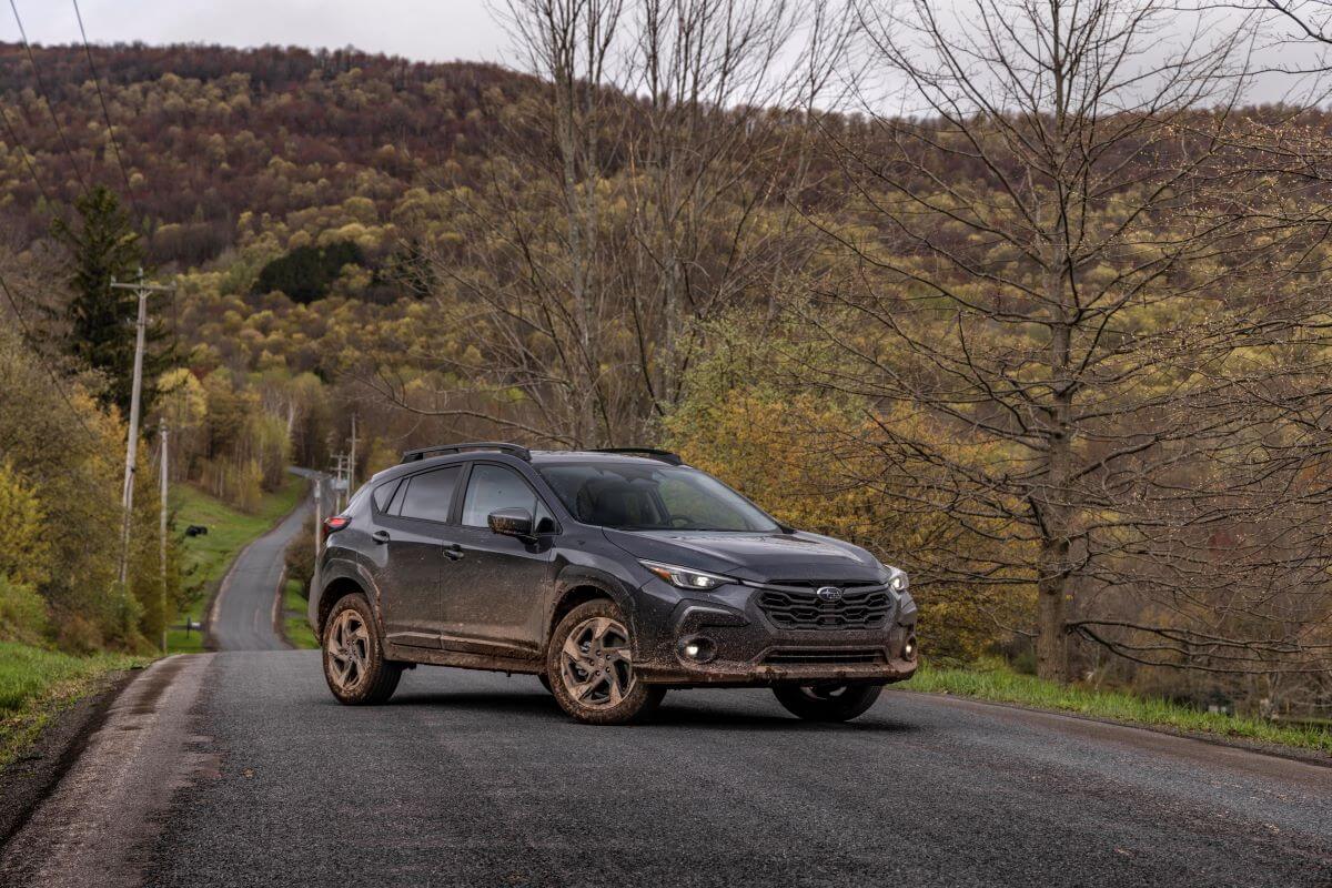 A 2024 Subaru Crosstrek compact SUV model caked in dirt and parked in the middle of a road near a yellow forest
