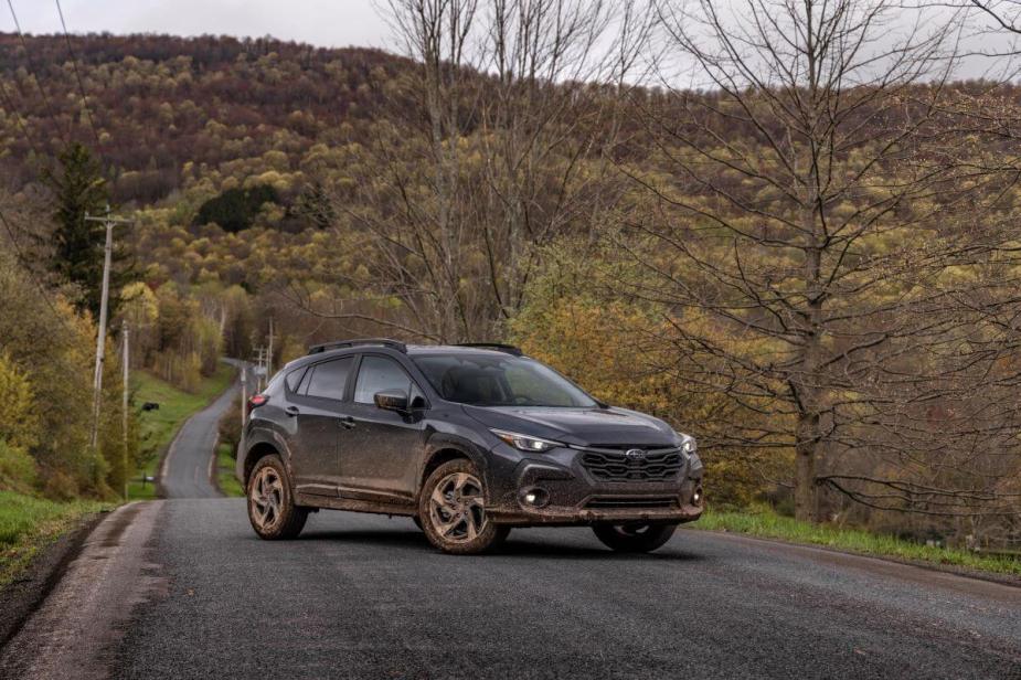 A 2024 Subaru Crosstrek compact SUV model caked in dirt and parked in the middle of a road near a yellow forest